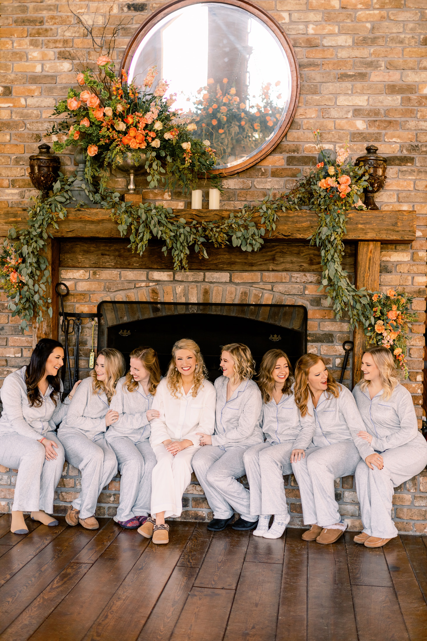 Bridesmaids in getting ready attire sitting in front of a fireplace decorated with floral arrangements