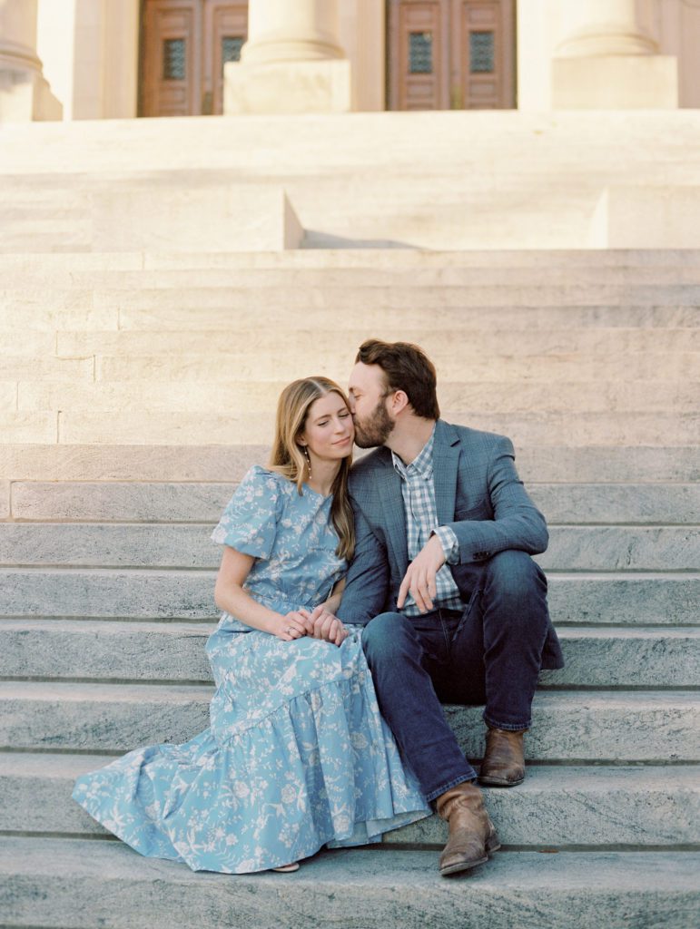 Sweet engaged couple taking photos on the steps of City Hall, Jackson Mississippi wearing a french blue cut out maxi dress and a grey suit with a gingham shirt.